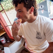 Man eating a donut with colorful sprinkles while holding a box of donuts.